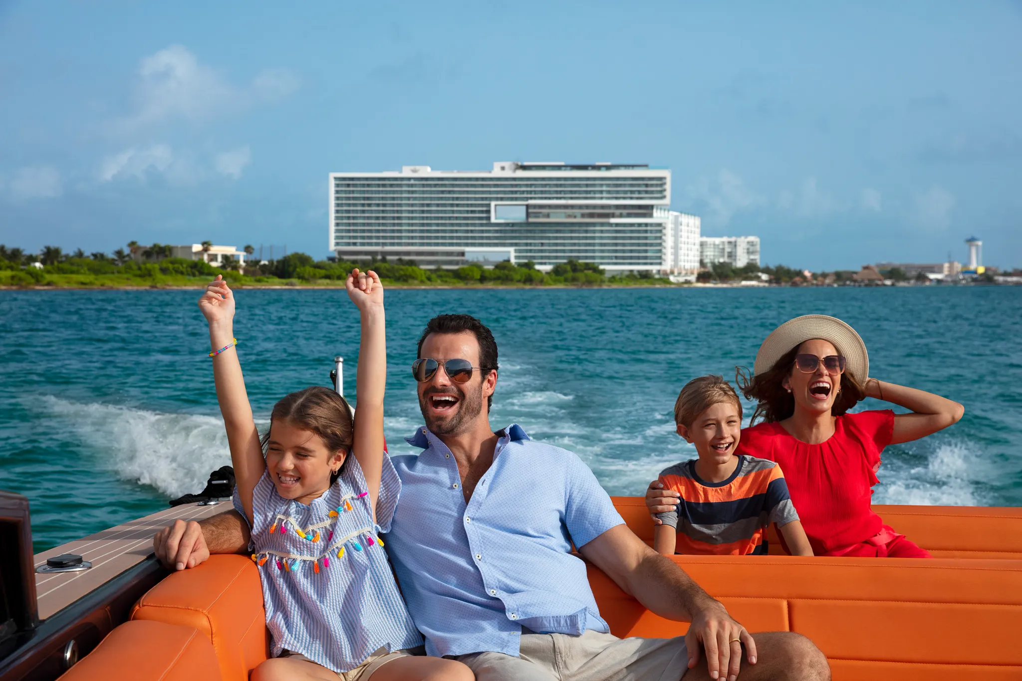 Family enjoying a speedboat ride near Dreams Vista Cancun Golf & Spa Resort with ocean views and resort in the distance.