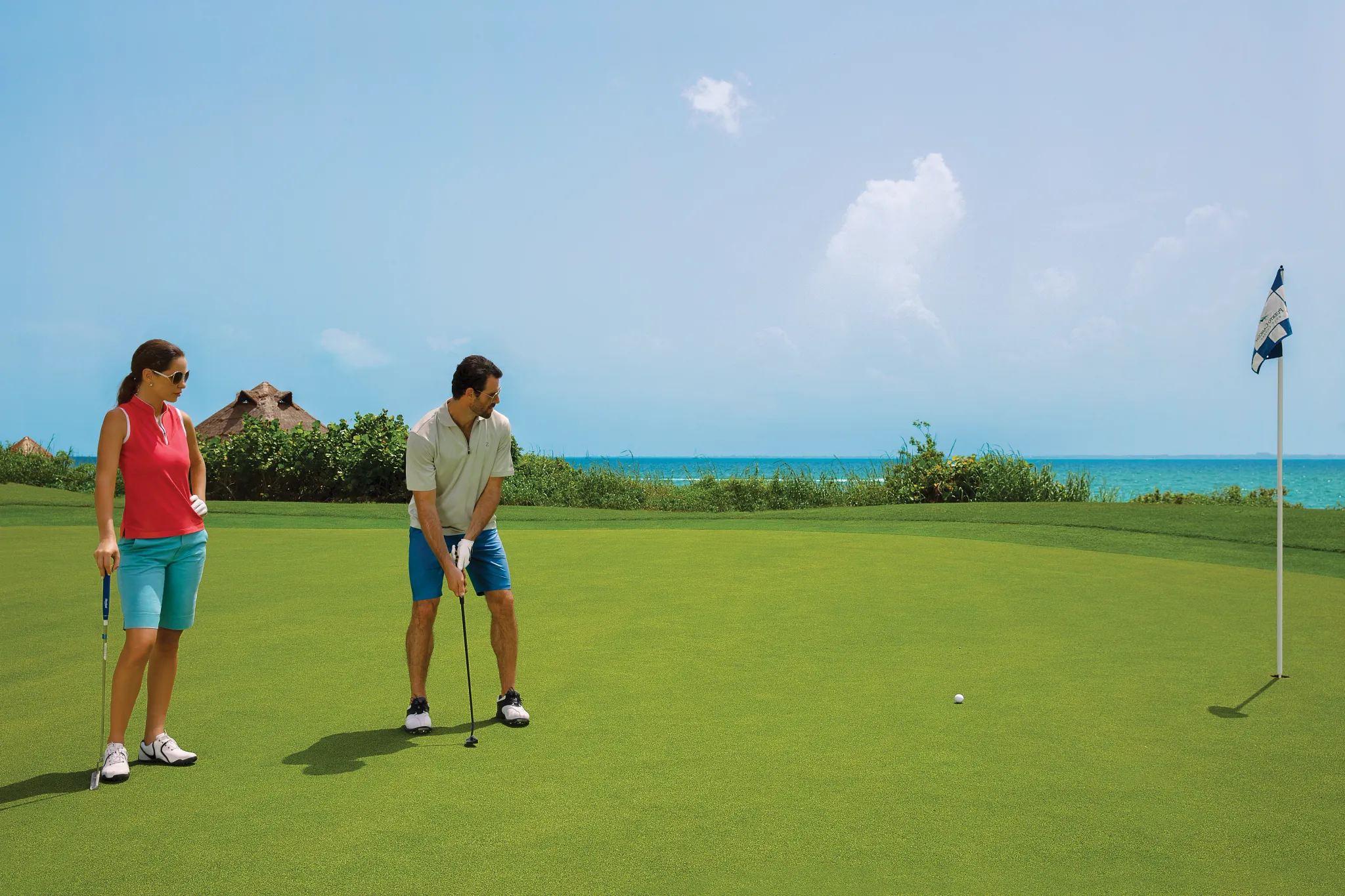 Couple playing golf near the ocean at Dreams Vista Cancun Golf & Spa Resort.